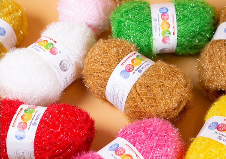 May include: Assortment of colorful scrubbers made of yarn. The scrubbers are in various colors, including white, pink, green, yellow, orange, and red. The scrubbers are all rolled up and have a label with the text "The Washing Companion" and "YECHOL" on them.