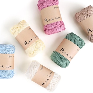 May include: A collection of colorful yarn skeins in shades of pink, blue, green, beige, and white. Each skein is wrapped with a brown paper band featuring the text "Modal hia". Ideal for knitting and crochet projects.