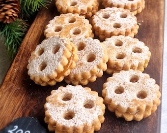 Peut inclure: Gros plan sur une planche en bois avec une variété de biscuits. Les biscuits sont ronds et de couleur brun clair. Ils sont recouverts de sucre glace et ont un trou au centre. Les biscuits sont disposés en cercle sur la planche.