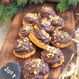 Op de afbeelding: Een close-up van een houten oppervlak met negen met chocolade bedekte koekjes, bedekt met knapperige kruimels. De koekjes zijn in een cirkelvormige opstelling geplaatst.