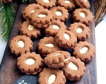 Peut inclure: Un assortiment de biscuits bruns en forme de fleur, garnis d'une garniture blanche et d'une amande blanche au centre, disposés sur une planche en bois. Les biscuits sont empilés, certains les uns sur les autres. Le chiffre "2009" est écrit sur une petite pierre sombre.