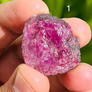 Puede incluir: Un cristal de rubí rojo intenso con una textura rugosa y natural. El cristal es aproximadamente del tamaño de una canica grande.