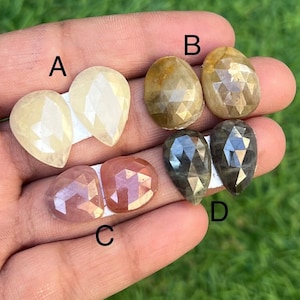 Op de afbeelding: Vier paar facetgeslepen edelsteen cabochons in verschillende kleuren, gelabeld A, B, C en D. De edelstenen zijn peervormig en hebben een facetgeslepen afwerking. De kleuren zijn wit, geel, roze en grijs.