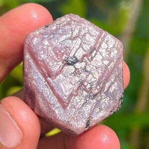 May include: A pink ruby crystal with a hexagonal shape and a sparkly, iridescent surface.