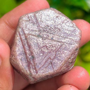 Puede incluir: Una piedra preciosa de rubí natural en bruto, facetada, rosa y plateada. El rubí tiene una forma hexagonal y mide aproximadamente 5 cm de diámetro.