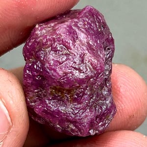 Puede incluir: Una gran gema de rubí rosa en bruto con un tono rojo intenso. El rubí tiene un acabado natural sin pulir.