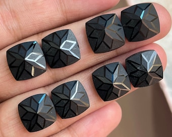 May include: Eight black gemstone cabochons with a star-shaped design. The cabochons are cut in a square shape with rounded edges.