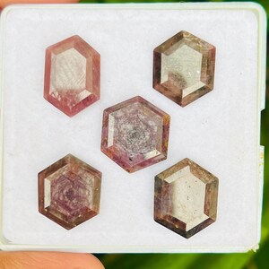 Peut inclure: Cinq pierres précieuses taillées en hexagone dans une boîte blanche. Les pierres précieuses sont un mélange de rose et de gris.