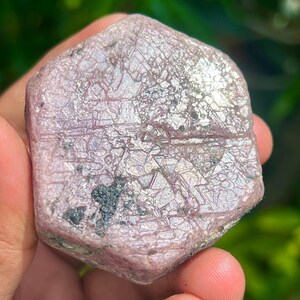 May include: A large, pink, hexagonal ruby crystal with a rough, textured surface. The crystal has a silvery sheen and is partially translucent.