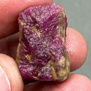 Può includere: Una pietra preziosa di rubino rosso grezzo con un colore profondo e ricco. Il rubino ha una finitura naturale non lucidata e mostra intricati motivi di inclusioni.