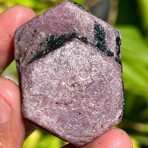 May include: A pink ruby crystal with black inclusions. The crystal is faceted and has a hexagonal shape.