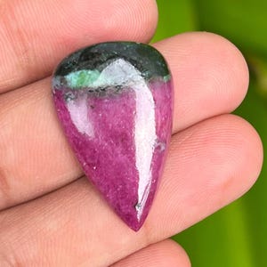 Op de afbeelding: Een traanvormige cabochon edelsteen met een groen en roze kleurenschema. De edelsteen is geslepen en gepolijst en heeft een glad, glanzend oppervlak.