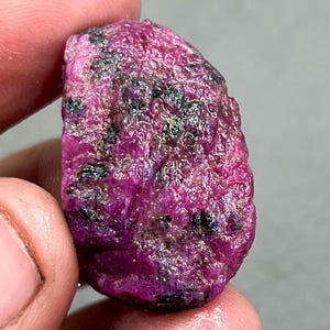 Op de afbeelding: Een ruwe, roze robijn edelsteen met zwarte insluitsels. De robijn is een natuurlijke, onbewerkte steen.