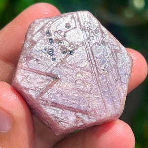 Könnte beinhalten: Ein rosa-weißer Edelstein mit sechseckiger Form und einer rauen, strukturierten Oberfläche. Der Edelstein hat ein natürliches, unpoliertes Aussehen und ist ein wunderschönes Beispiel für einen rohen Kristall.