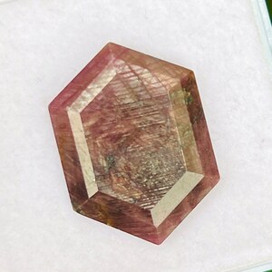 May include: A faceted, hexagonal, pink and brown gemstone with a striated pattern.