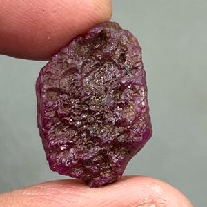 Puede incluir: Una piedra preciosa de rubí rosa oscuro en bruto con un acabado natural sin pulir.