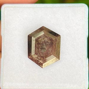 Peut inclure: Une pierre précieuse taillée en hexagone de couleur brune et violette. La pierre précieuse est présentée dans une boîte blanche.