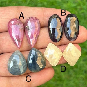 Puede incluir: Seis cabujones de piedra preciosa facetados, dos de cada color: rosa, negro y amarillo. Las piedras están etiquetadas como A, B, C y D.