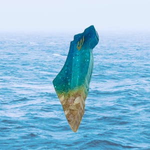 May include: A resin sculpture in the shape of a country, featuring layers of blue and turquoise resin with glitter, resembling water. The bottom section has a sandy, textured appearance. A gold emblem is visible at the top.