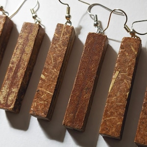 May include: A close-up shot of several rectangular wooden earrings with silver-colored fish hook ear wires. The earrings are a warm brown color with visible wood grain and texture. The earrings are displayed against a white background.