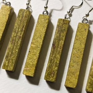 May include: A set of handmade earrings featuring rectangular, light green and brown wooden beads. The earrings have silver-colored fish hook ear wires. The wooden beads have a textured, natural appearance.