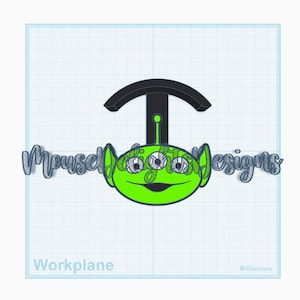 May include: A green alien face with three eyes, a black antenna, and a smiling mouth. The text "Mousell Designs" is written in a cursive font. The word "Workplane" is written at the bottom.