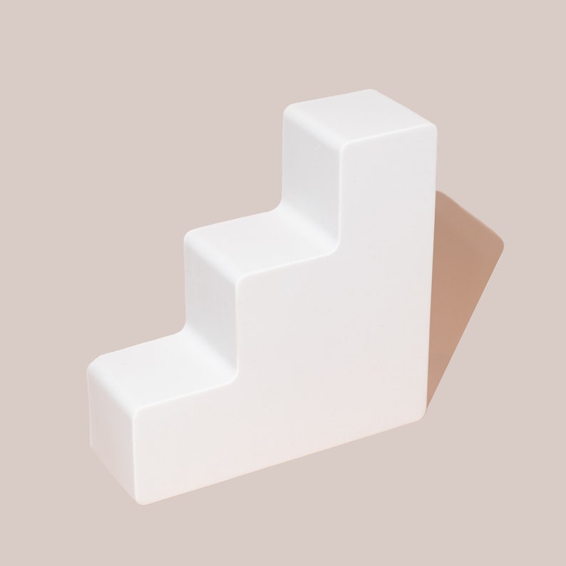Op de afbeelding: Witte drietrapsplatform gemaakt van glad, massief materiaal. Het platform is lichtjes naar rechts gekanteld.