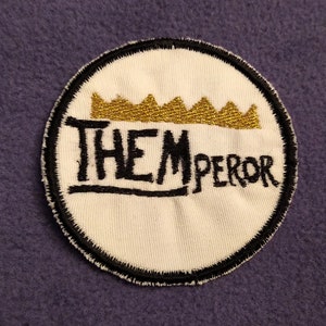 May include: A white embroidered patch with a black outline and a gold crown above the text "THEMPEROR".