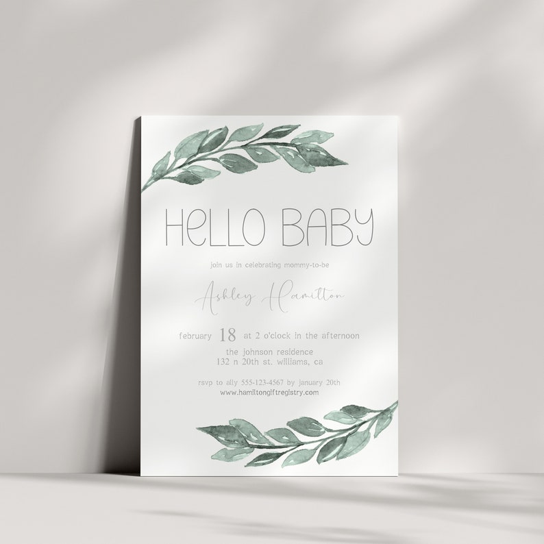 K&ouml;nnte beinhalten: Eine Babyparty-Einladung mit einer Aquarell-Illustration von gr&uuml;nen Bl&auml;ttern und dem Text "HELLO BABY". Die Einladung ist f&uuml;r Ashley Hamilton und enth&auml;lt Datum, Uhrzeit und Ort der Party. RSVP-Informationen sind ebenfalls enthalten.