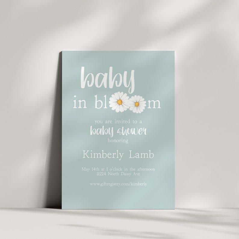 Puede incluir: Una invitaci&oacute;n de color azul claro para un baby shower con texto blanco que dice "baby in bloom" con dos margaritas blancas con centros amarillos. La invitaci&oacute;n tambi&eacute;n incluye el texto "est&aacute;s invitado a un baby shower en honor a Kimberly Lamb" y la fecha, hora y lugar del baby shower. La invitaci&oacute;n tambi&eacute;n incluye una direcci&oacute;n de sitio web para el registro de regalos.