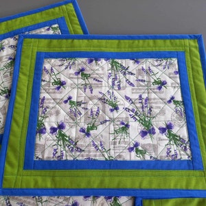 Könnte beinhalten: Set mit drei gequilteten Platzsets mit einem Lavendel-Blumendruck. Die Platzsets haben einen grünen und blauen Rand.