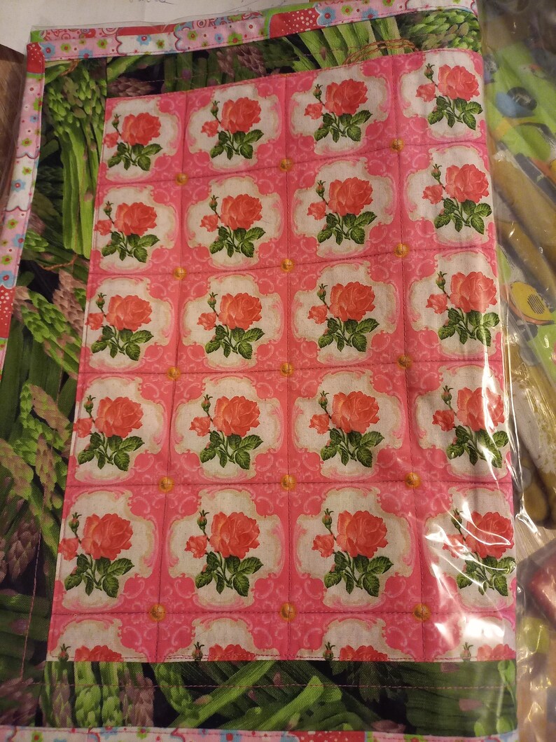 May include: A pink fabric panel with a repeating pattern of pink roses in white and green frames. The fabric is quilted and has a green and white border.