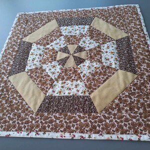 Könnte beinhalten: Ein brauner und beigefarbener Patchwork-Deckenbezug mit Blumenmuster. Der Bezug besteht aus Quadraten und Dreiecken und hat einen weißen Rand.