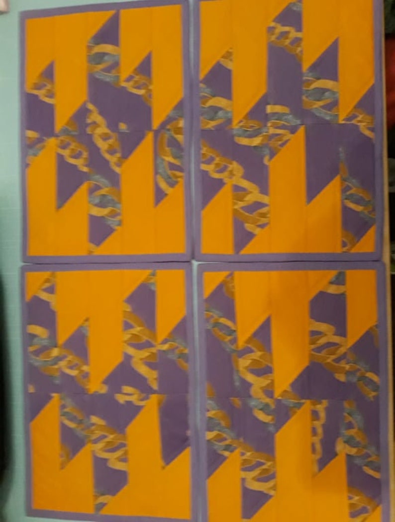 May include: Four placemats with a geometric pattern of purple and orange. The pattern is made up of overlapping triangles and rectangles.