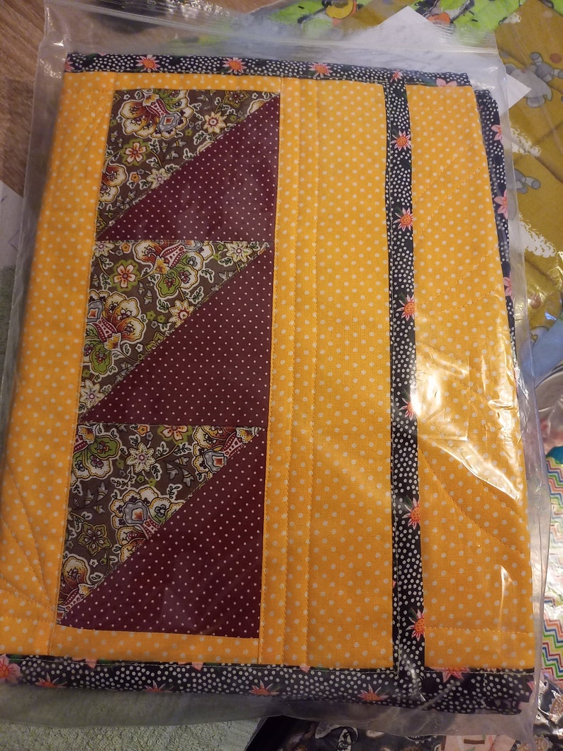 K&ouml;nnte beinhalten: Ein gesteppter Tischl&auml;ufer mit gelbem Hintergrund und einem burgunderfarbenen und floralen Muster. Der L&auml;ufer hat einen schwarzen und wei&szlig;en Besatz mit kleinen floralen Akzenten.
