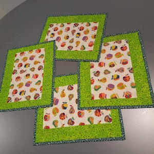 Könnte beinhalten: Vier grüne und weiße gesteppte Tischsets mit einem Fruchtmuster. Die Tischsets haben einen grünen Rand und eine weiße Mitte mit einem Muster aus bunten Birnen, Äpfeln und Pflaumen.