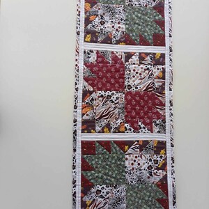 Könnte beinhalten: Ein gesteppter Tischläufer mit Patchwork-Design aus braunen, grünen, weißen und roten Stoffen. Der Läufer hat ein geometrisches Muster mit einem Sternendesign.