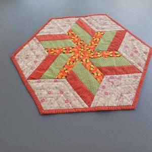 Könnte beinhalten: Ein sechseckiger Tischläufer mit einem Sternmuster in Orange-, Grün- und Weißtönen. Der Läufer besteht aus Patchwork-Stoff mit verschiedenen Blumenmustern.