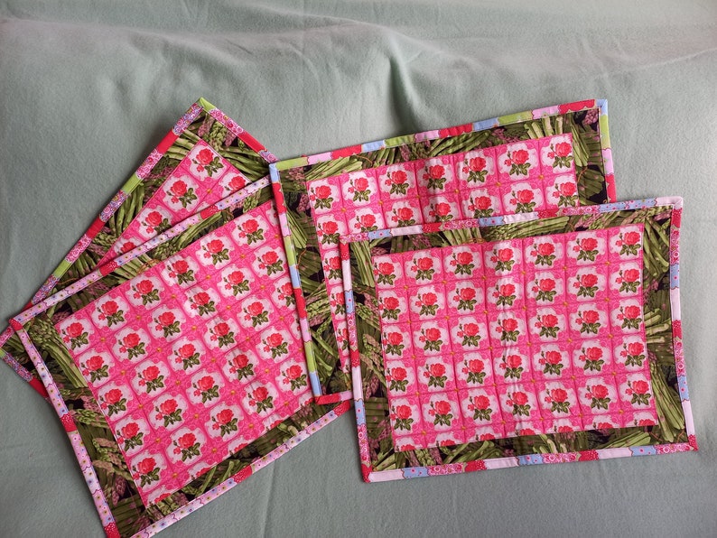May include: Four pink and green quilted placemats with a floral pattern. The placemats have a multi-coloured trim.