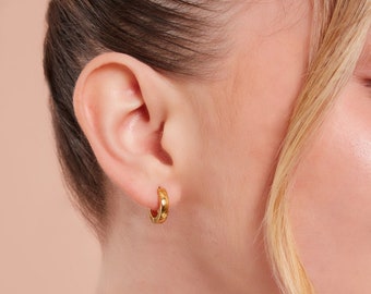Op de afbeelding: Gouden creolen met een gedraaid ontwerp. De oorbellen worden gedragen door een persoon met blond haar.