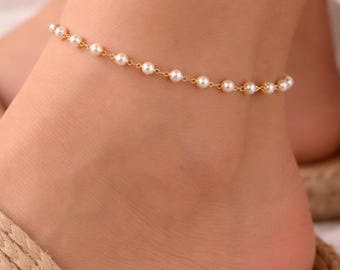 May include: A delicate gold chain anklet featuring a series of evenly spaced, small, round, white pearls. The anklet is secured around the ankle, showcasing a minimalist design with a thin metallic link chain and lustrous pearl accents.
