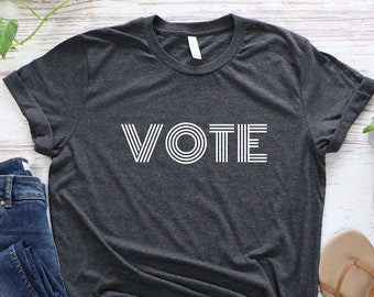May include: A dark gray t-shirt with the word "VOTE" printed in white on the front. The letters are made up of white lines.