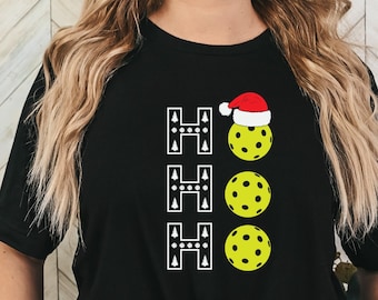 Könnte beinhalten: Schwarzes T-Shirt mit einem weißen "HO HO HO"-Design mit einer Weihnachtsmütze und drei gelben Pickleball-Bällen.