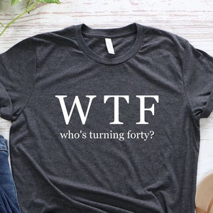K&ouml;nnte beinhalten: Ein dunkelgraues T-Shirt mit dem Aufdruck "WTF who's turning forty?" in wei&szlig;.