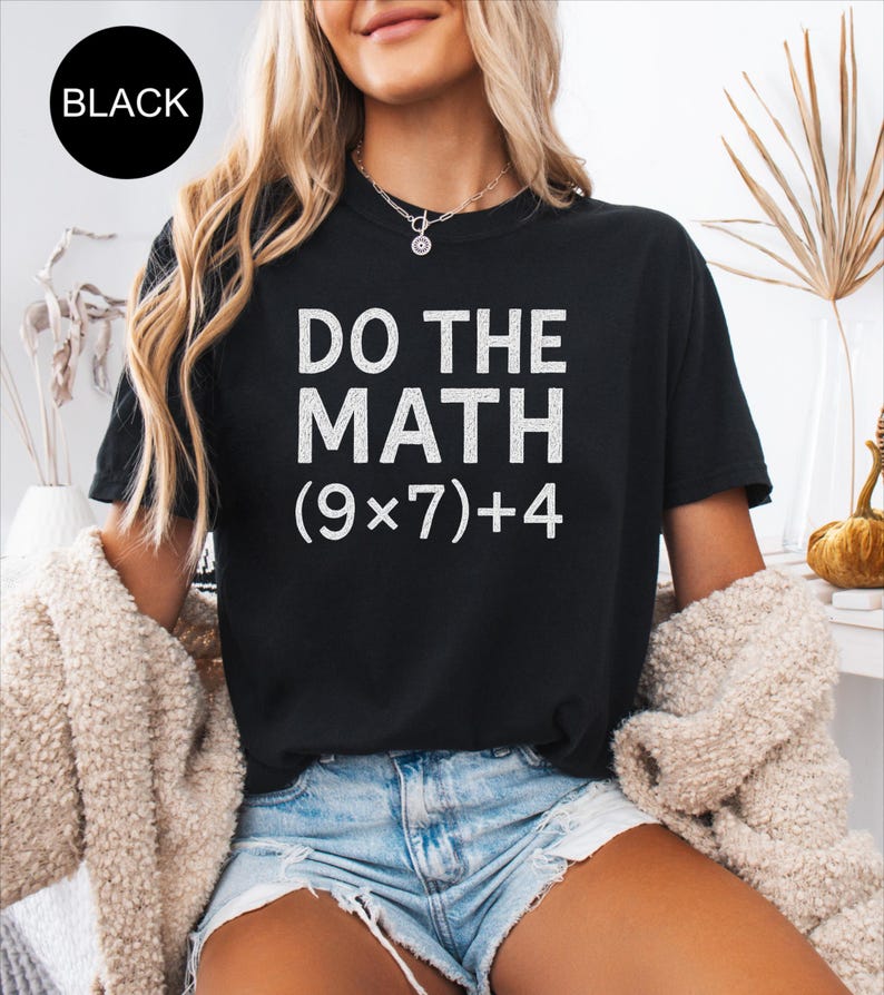 May include: Black t-shirt with the text "DO THE MATH (9x7)+4" in white. The shirt is a crew neck style and is being worn with denim shorts. A black circle with the word "BLACK" is in the upper left corner.