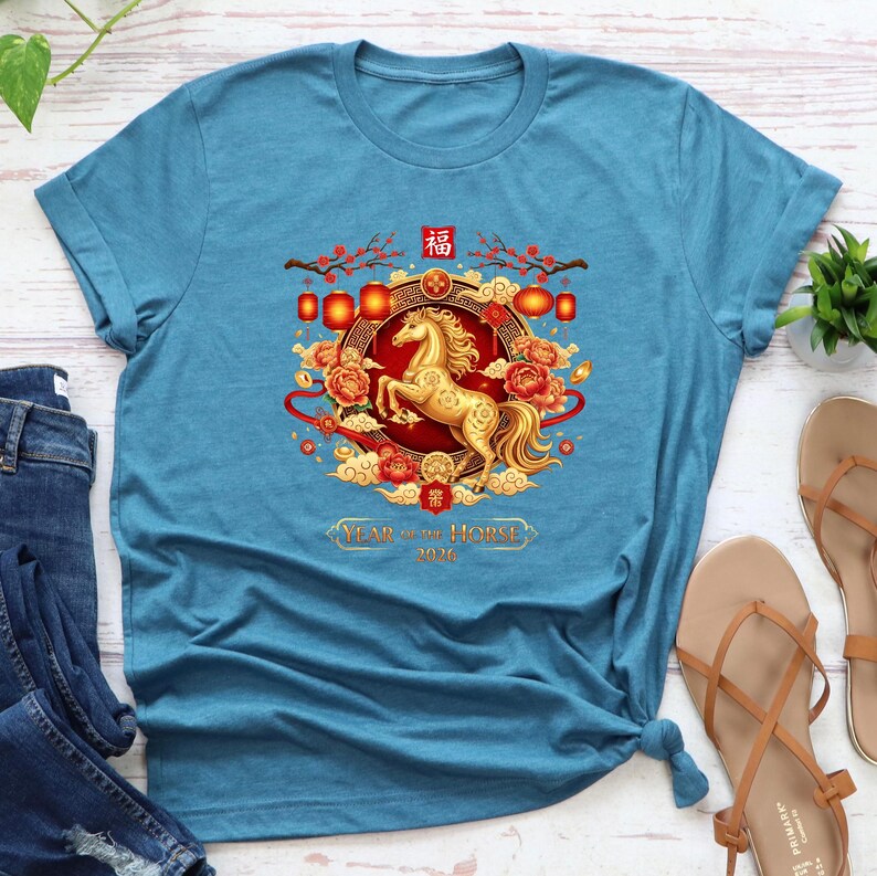 May include: A teal t-shirt featuring a golden horse design within a circular frame. The design includes red lanterns, flowers, and the text "Year of the Horse 2026". The shirt is a casual wear item.