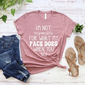 May include: A mauve t-shirt with the text "I'm not responsible for what my face does when you talk" in white lettering.