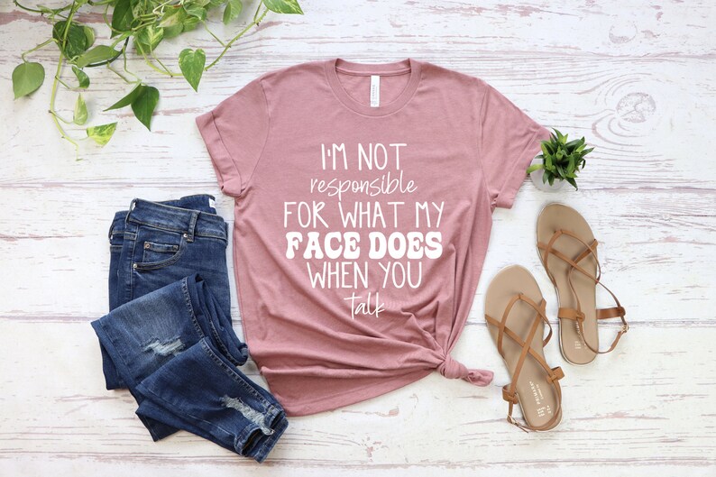 May include: A mauve t-shirt with the text "I'm not responsible for what my face does when you talk" in white lettering.