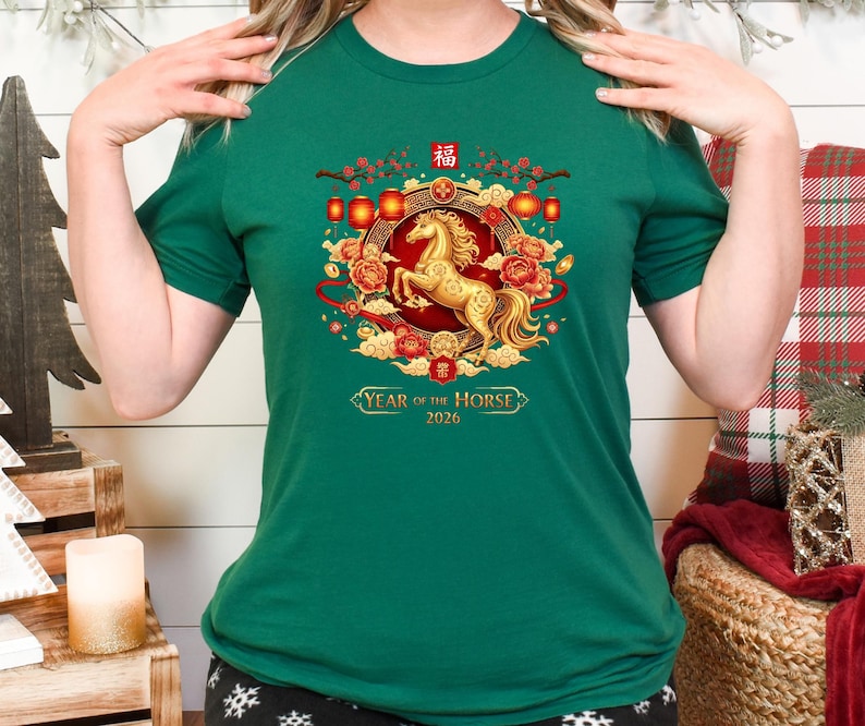May include: A green t-shirt featuring a golden horse design, surrounded by red and gold floral elements and lanterns. The text "Year of the Horse 2026" is displayed below the horse. The shirt is a short-sleeved crew neck.