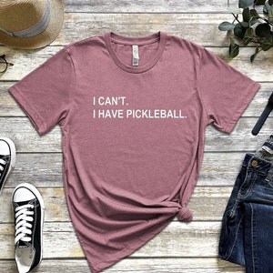 May include: A mauve t-shirt with the text "I CAN'T. I HAVE PICKLEBALL." printed in white.